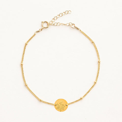 Gold birth flower bracelet by Gratinsta featuring delicate floral charms on a fine gold chain.