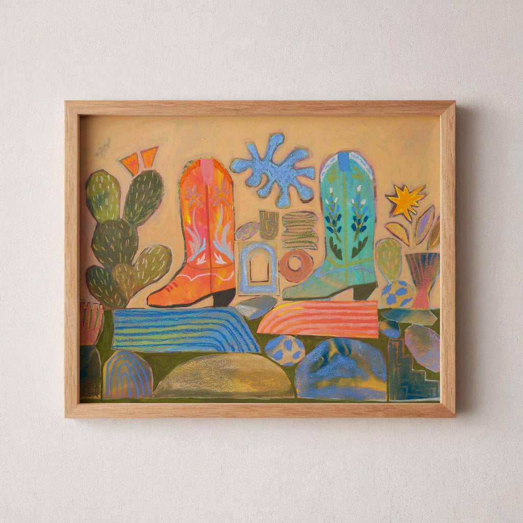 Framed colorful abstract artwork with cowboy boots, cactus, and other elements on a beige wall.