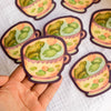 Colorful frog vinyl sticker from Wild Pencil Studio featuring a playful frog design for decorating notebooks and laptops.