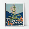 A framed art print featuring an abstract painting of a green plant with pale flowers against a light blue sky and dark blue hills, leaning against a white wall.