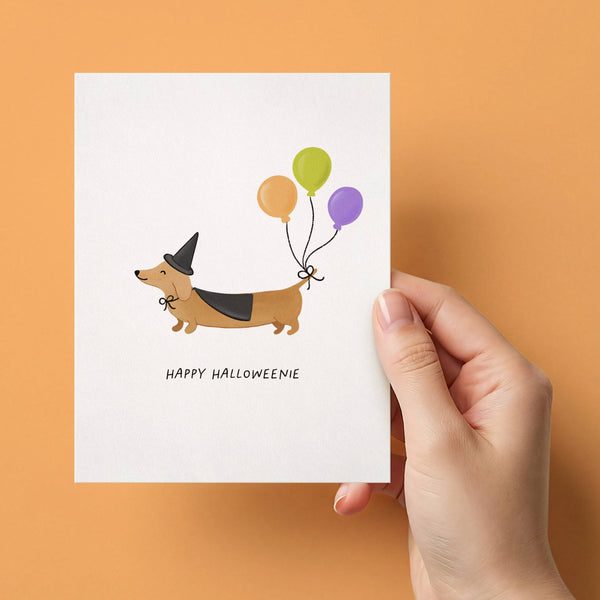 Happy Halloweenie dog greeting card by Isabella MG featuring a festive Halloween-themed design with a cute dog illustration.