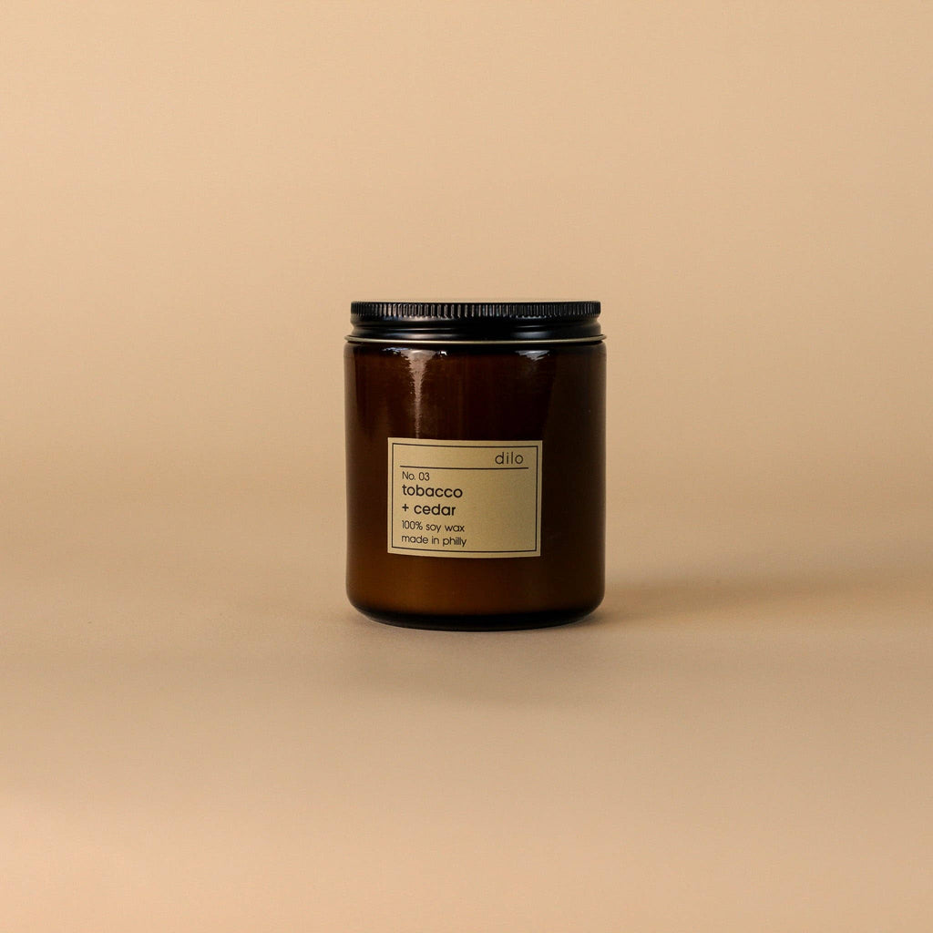 Dilo No. 03 Tobacco + Cedar candle in a glass holder, showcasing the warm, earthy scent and rustic design of the candle.