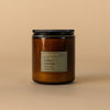 Dilo No. 02 Amber + Oakmoss candle with a sleek glass holder and lit wick, showcasing warm amber and earthy green moss fragrance.
