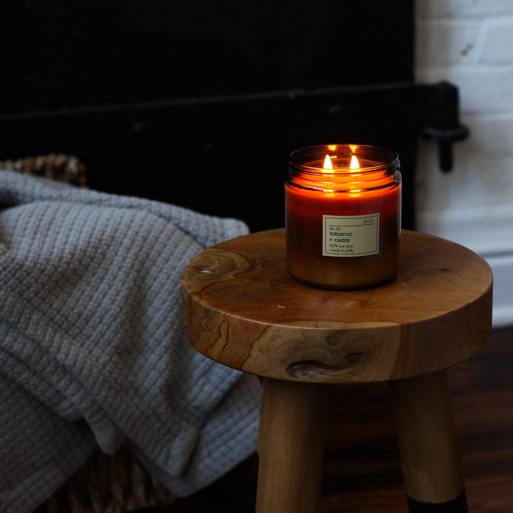 Dilo No. 03 Tobacco + Cedar candle in a glass holder, featuring warm amber wax and a wooden wick, ideal for cozy ambiance.