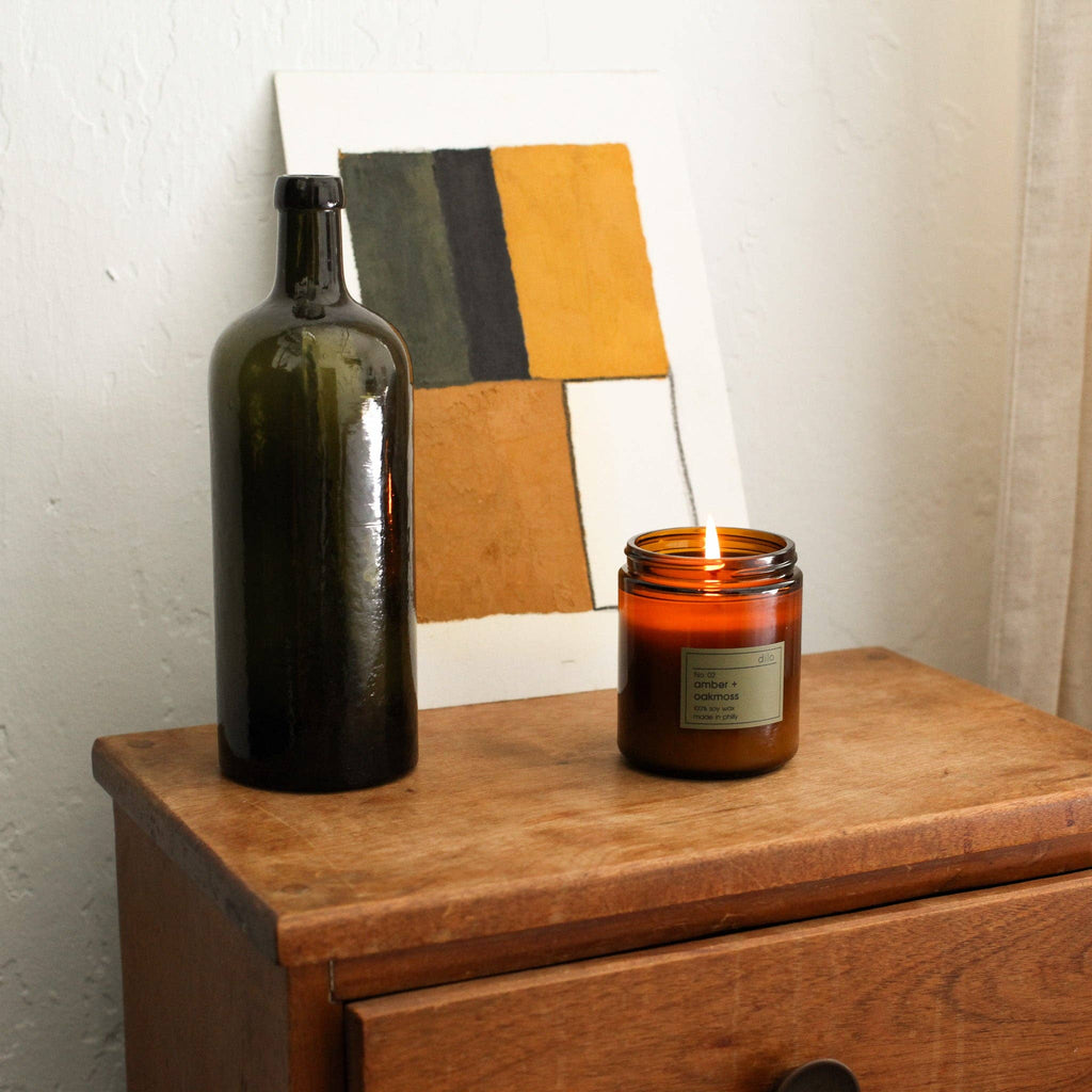Dilo No. 02 Amber + Oakmoss candle with a lit wick, in a glass jar, emitting warm amber and earthy oakmoss scents.
