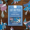 East End Press Garland book surrounded by decorative cut-out figures on a wooden surface