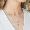 Gold necklace with a blue pendant worn by a person against a white background