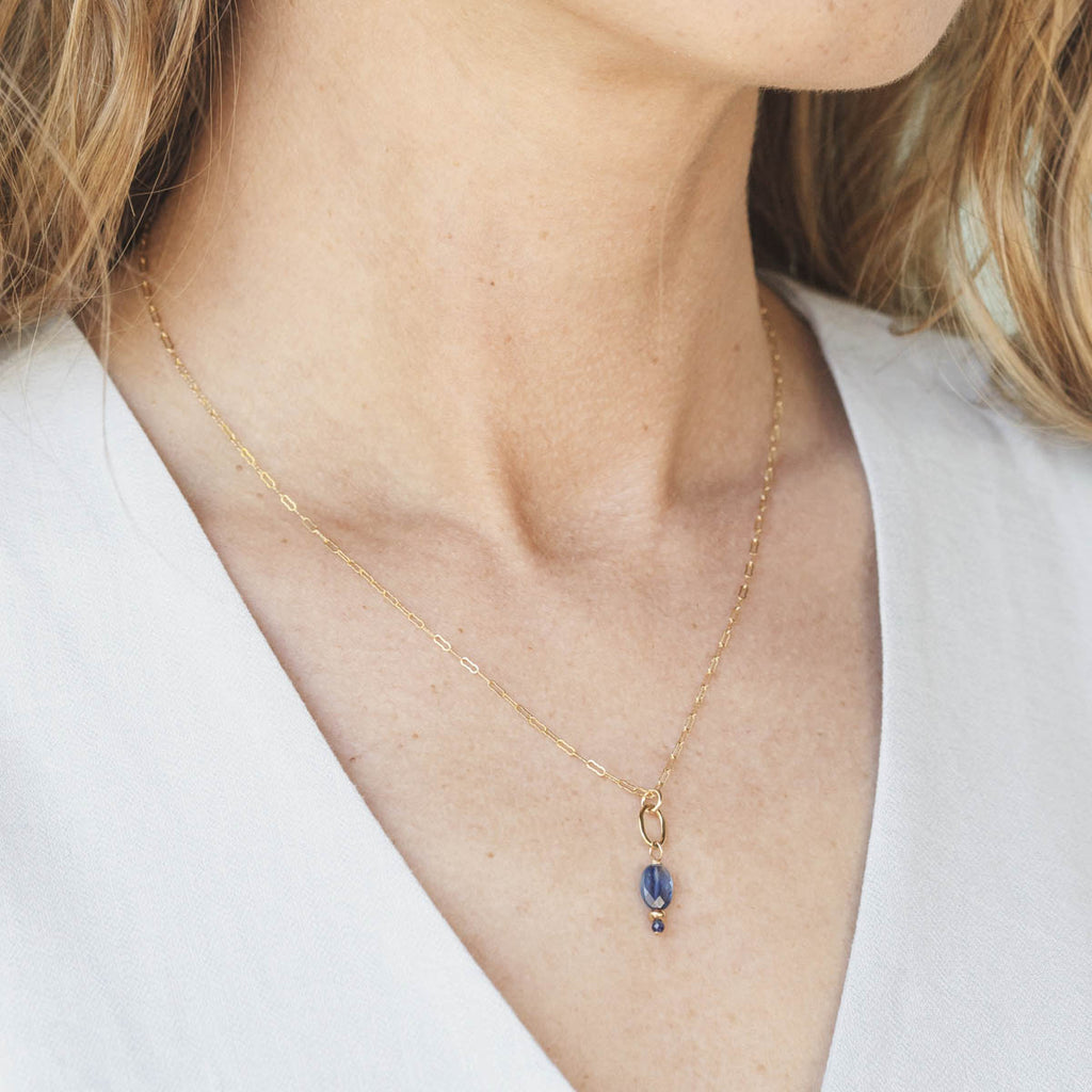 Gold necklace with a blue pendant worn by a person against a white background