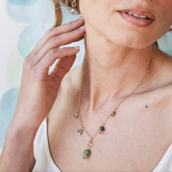 Woman wearing a delicate gold necklace with green beads against a soft, blurred background