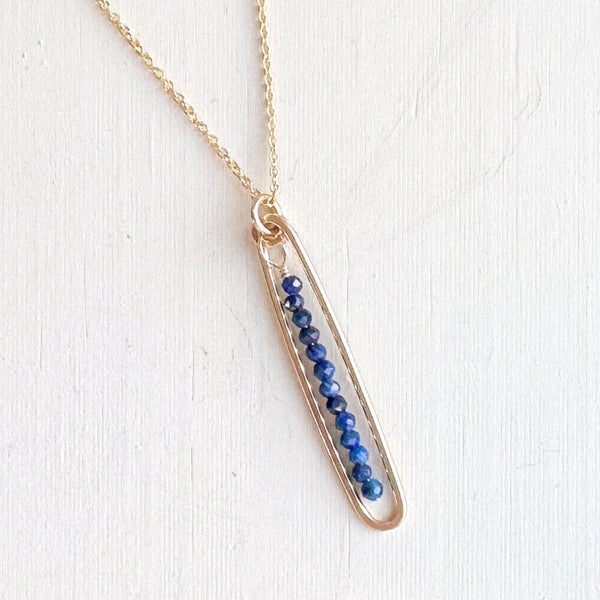 Gold necklace with a bar pendant featuring blue stones on a white background