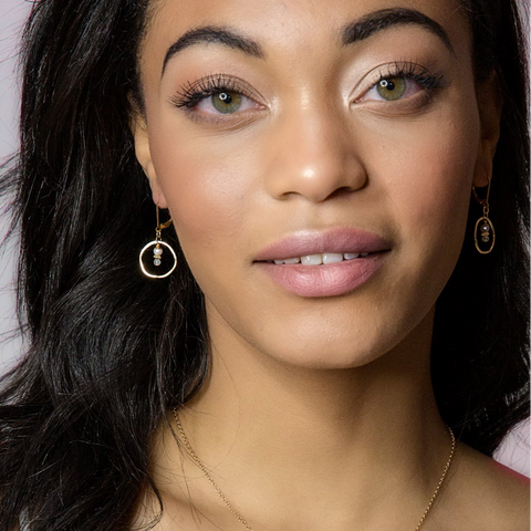 Sunrise Moonstone and gold circle earrings with sunset and dusky coast background, showcasing elegant jewelry design.